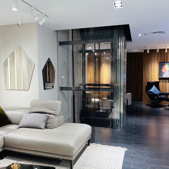 Glass lift behind a sofa and lounge chairs