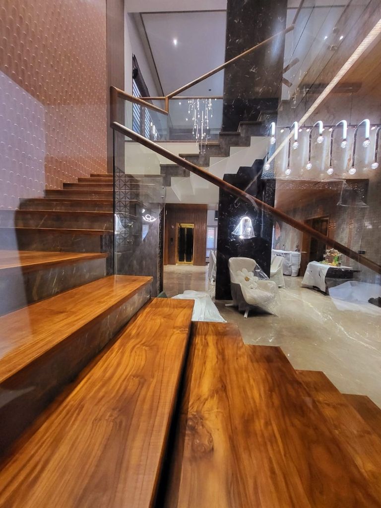 Teak staircase in a marble hall with the gold lift doors in the distance