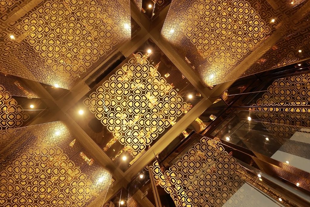 Gold cut-work cabin walls and ceiling lights, looking up inside the lift
