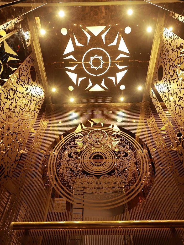 Gold lift cabin with a white cut-work star pattern on the ceiling and a mandala wall