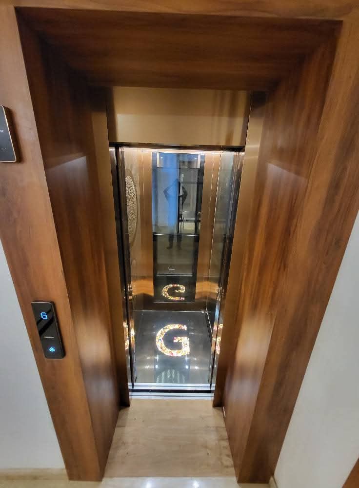 Lift doorway in a wooden surround opening onto a glass cabin with a lit floor